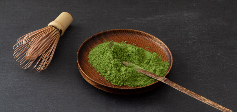 Matcha powder on a wooden plate with matcha whisk and spatula